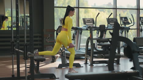 Sportive-woman-is-doing-lunges-for-legs-with-dumbbells-in-her-hands-in-gym.-Young-muscular-hispanic-woman-doing-Lunges-exercise-with-dumbbells-in-the-gym-In-yellow-sportswear